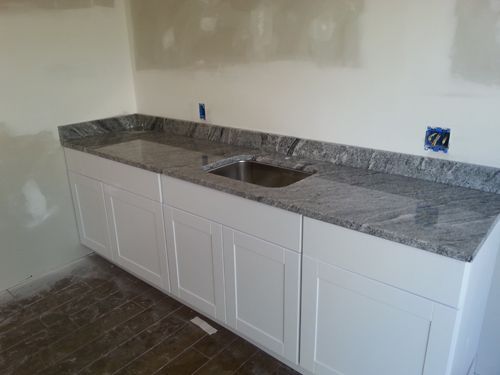 White cabinets with granite countertop and sink against a neutral wall; construction in progress.