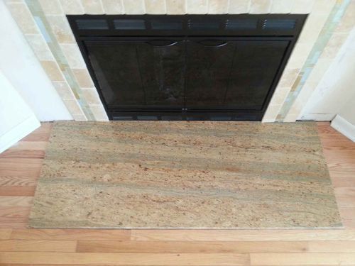 Fireplace with a granite hearth. The fireplace has dark doors and is surrounded by tan and cream tiles.