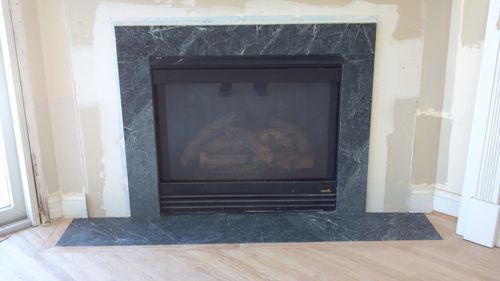 Fireplace with dark marble surround, against light walls and wooden floor.