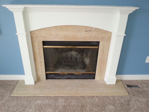 Fireplace with white mantel, tan stone surround, and black firebox.