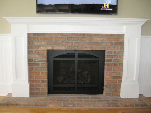 Brick fireplace with white mantel and black screen. A TV is above the mantel.