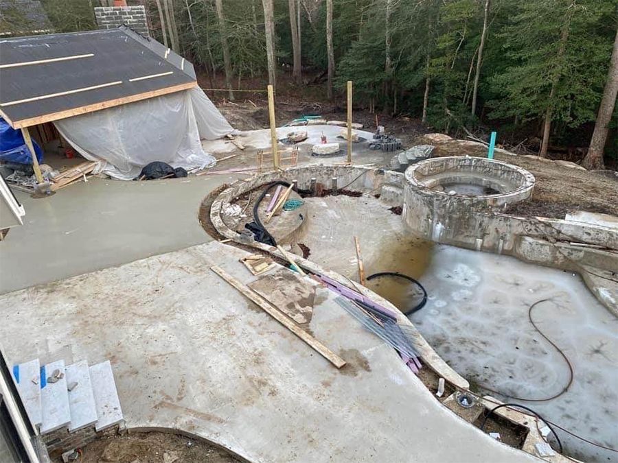 Construction site: concrete patio, steps, curved edges, circular spa, surrounding forest.