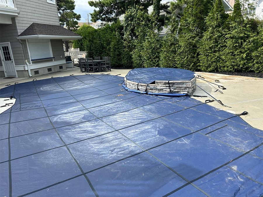 Blue pool cover on a concrete patio with a small above-ground pool; backyard setting.