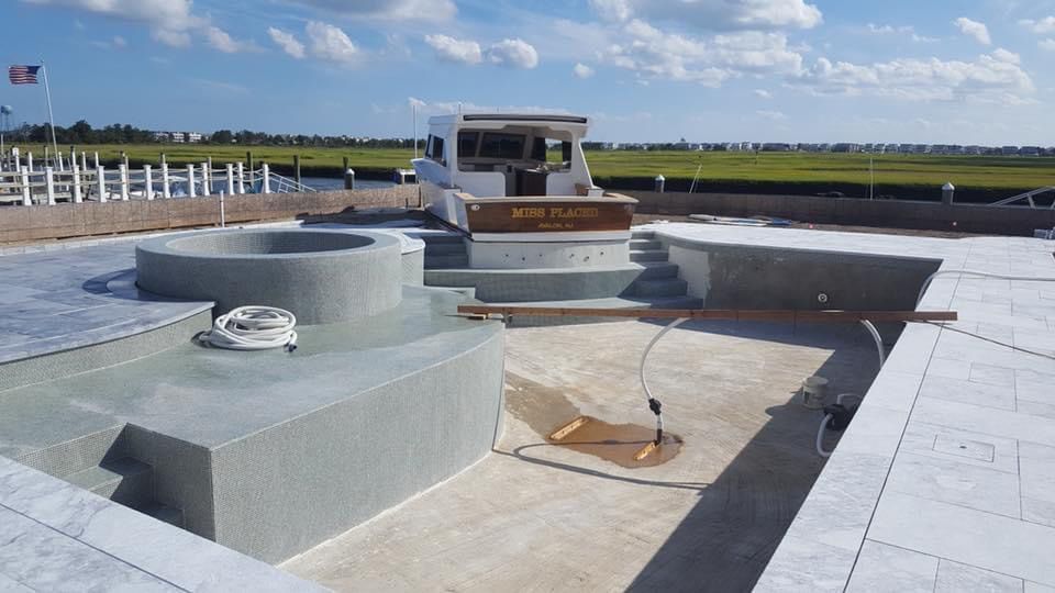 An unfinished pool deck with boat and grass in the background under a blue sky.