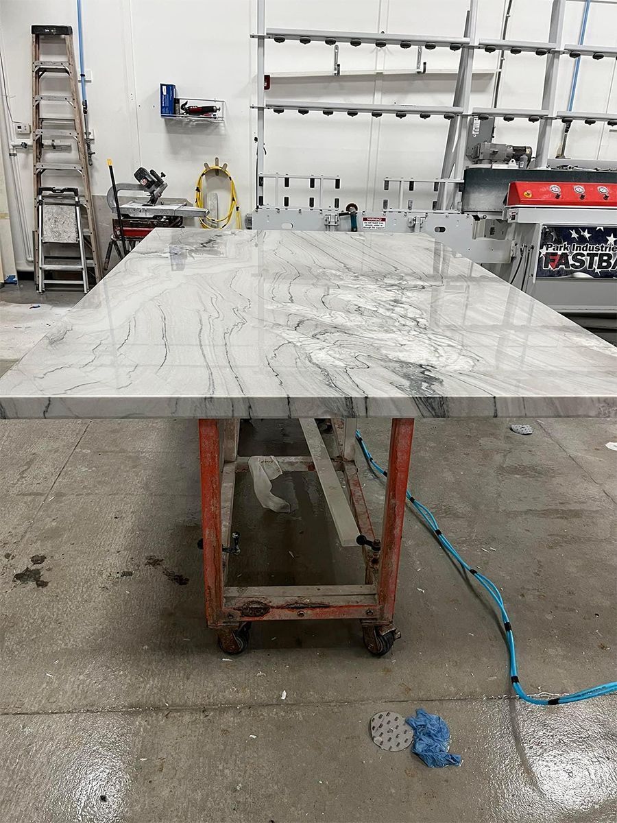 A large, light-colored granite countertop on a red cart in a workshop. A blue hose lies near the floor.