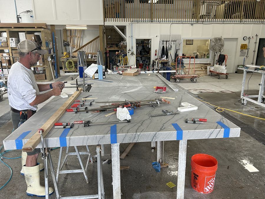 Man working on a large stone countertop in a workshop, using clamps and tools.