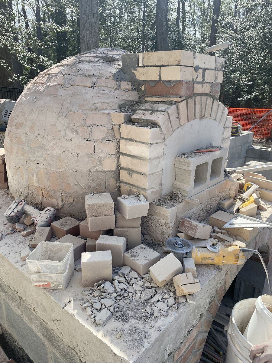 Outdoor brick oven under construction with scattered bricks and tools.