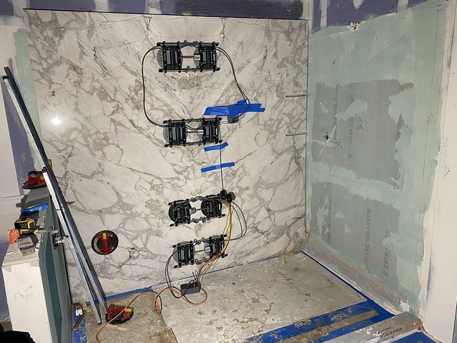 Shower wall with marble-patterned tile, electrical boxes wired, unfinished drywall, and construction tools.