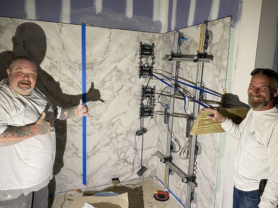 Two men pose in a bathroom with installed marble and bracing system; one gives a thumbs up.
