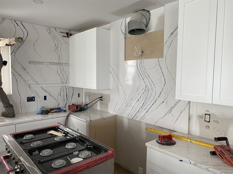 Kitchen under construction with white cabinets, marble-look backsplash, range, and a worker.