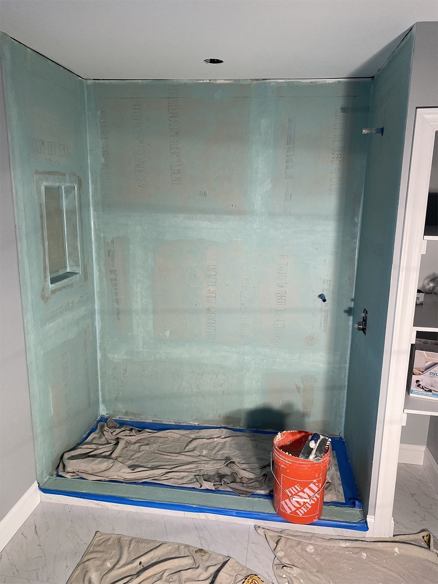 A shower enclosure with greenish-blue walls, prepared for tiling, featuring a window and a bucket.