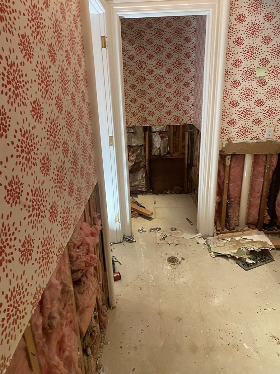 Room with damaged walls, exposed insulation and studs, floral wallpaper, doorway visible.