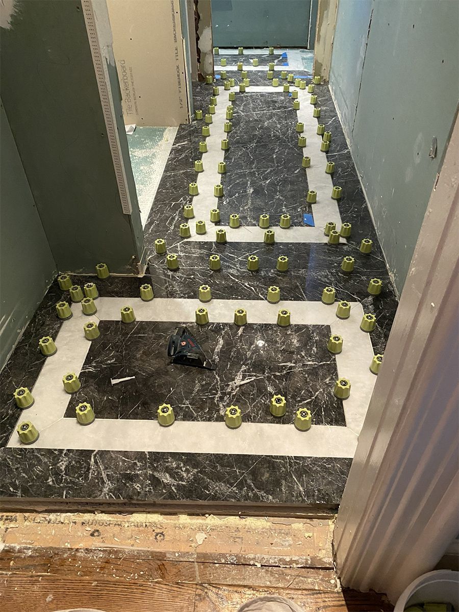 Tile floor installation in progress, green leveling spacers between black and white tiles, hallway setting.