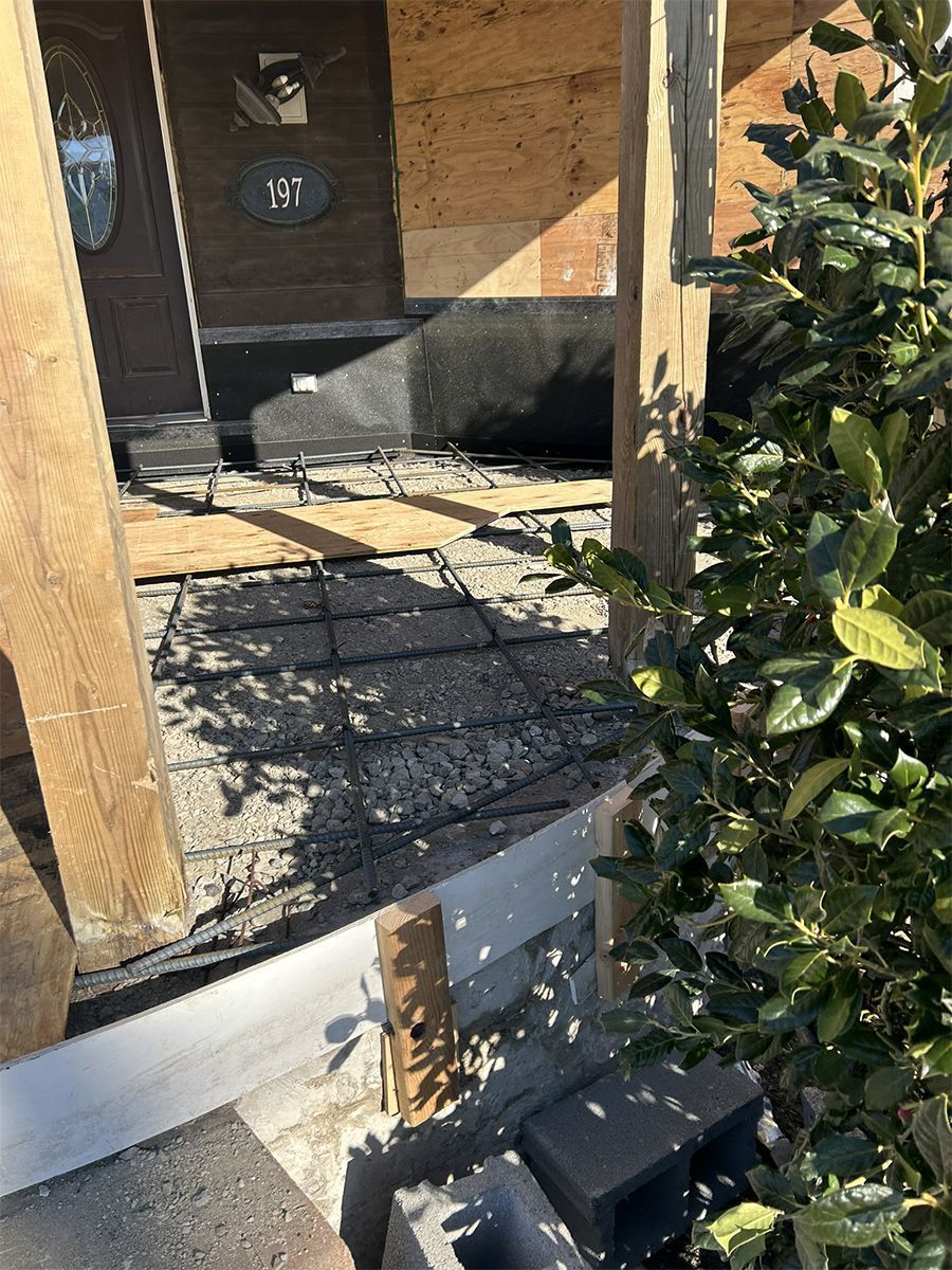 Construction site: partially built structure with exposed wood, shingles, and a bush on the right.