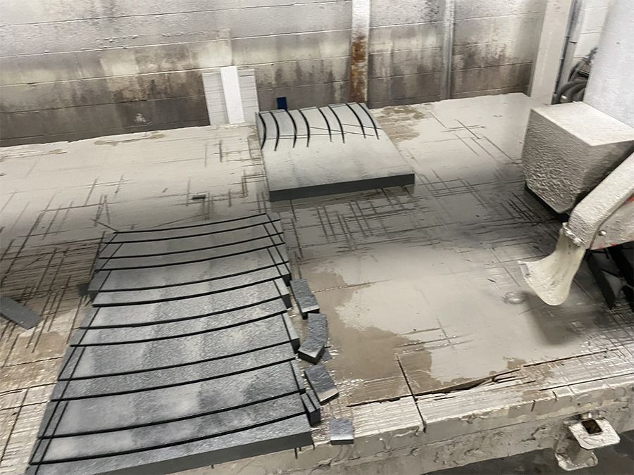 Gray stone slabs on a wet workbench, cut into curved shapes with a water jet. Industrial setting.