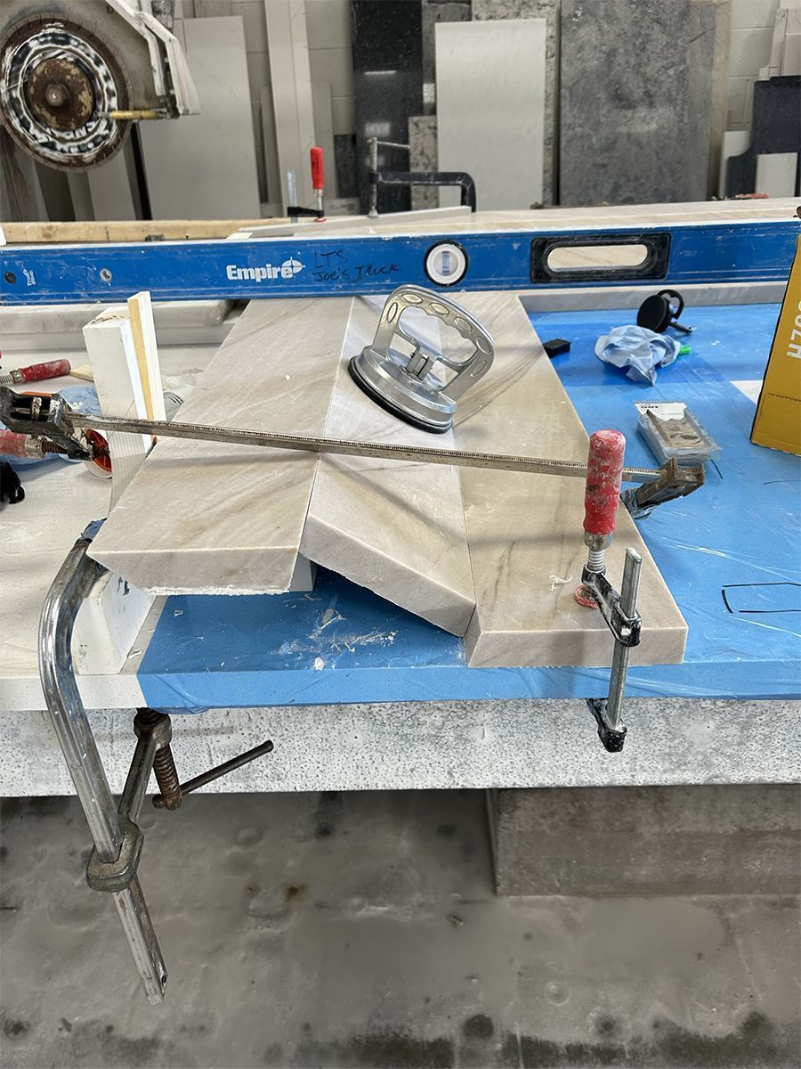 Marble countertop being assembled with clamps, level, and power tool on a work surface.