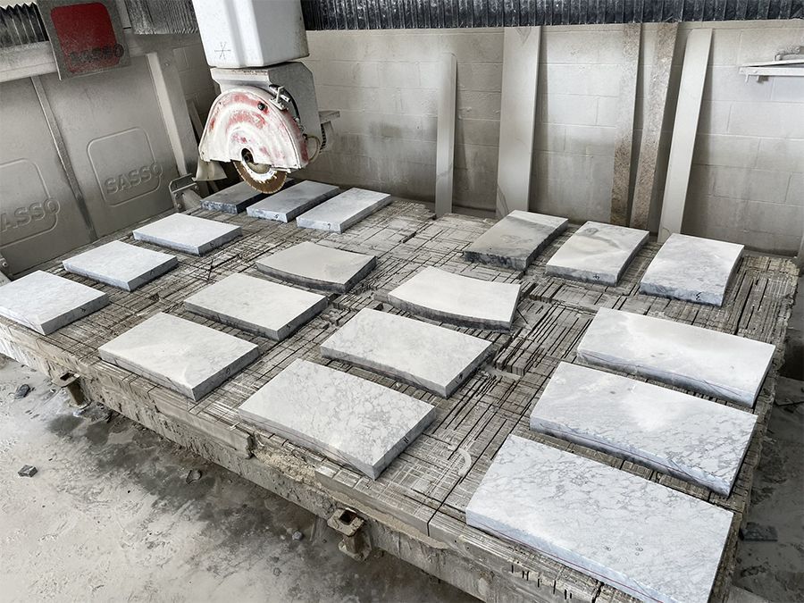 A saw cutting stone tiles on a metal table, with several tiles already cut.