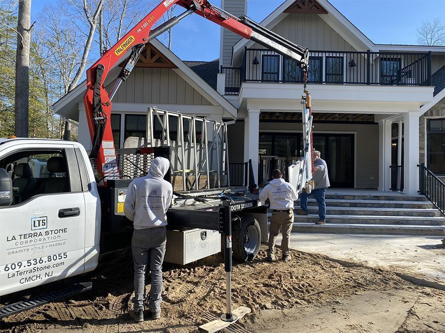 Truck with crane lifting window frame at a house under construction. Workers in gray hoodies assist.