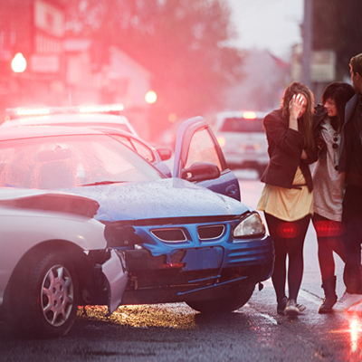 A group of people are standing next to a car that has been involved in a car accident.