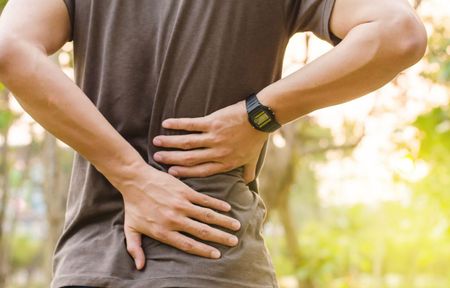 A man is holding his back in pain while wearing a watch.