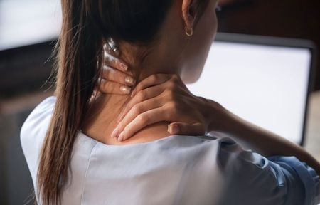 A woman is holding her neck in pain while sitting in front of a computer.