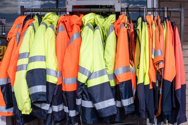 High-visibility work jackets, yellow and orange, hanging on a rack. Reflective stripes are visible.