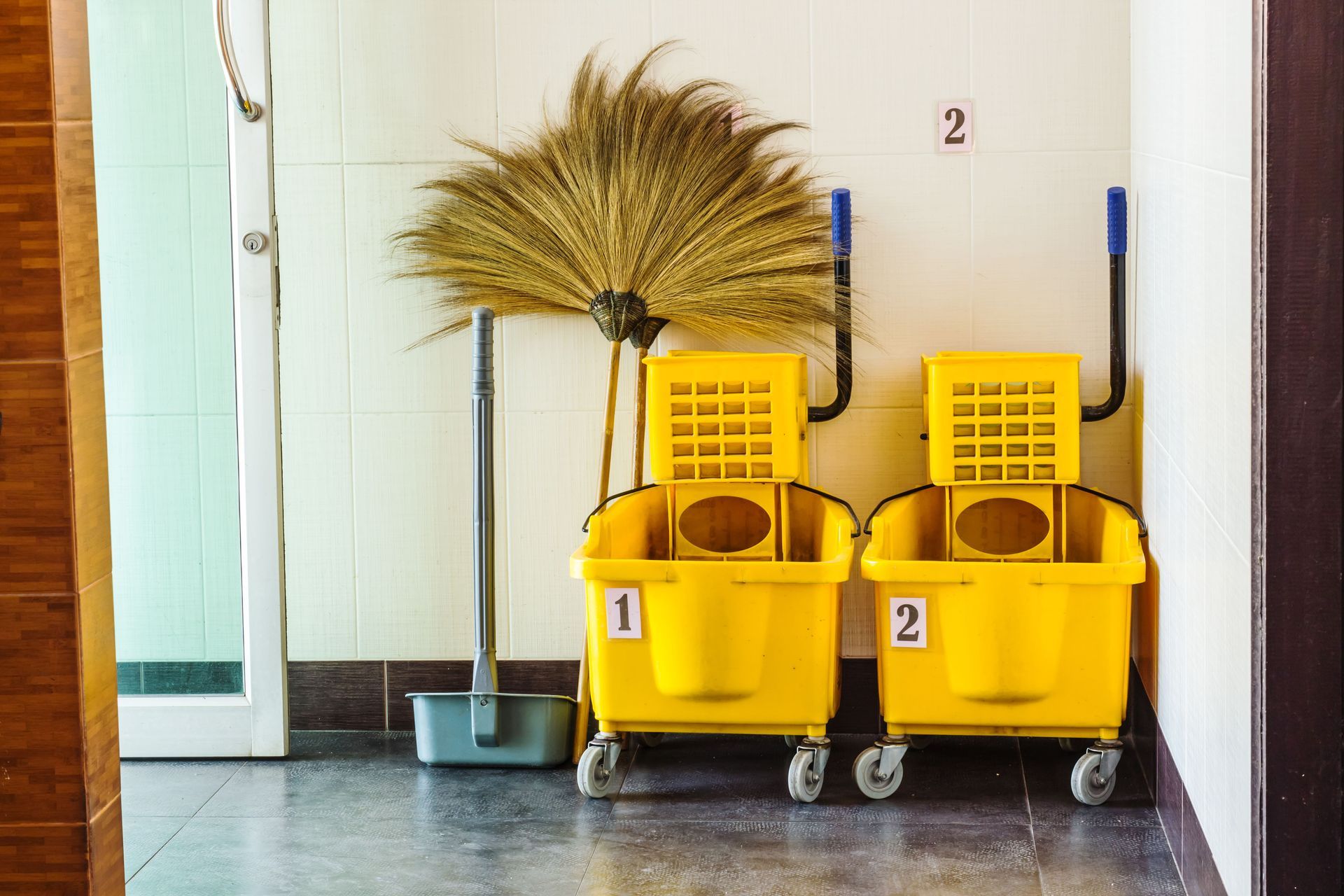 Yellow cleaning carts and broom in a hallway.
