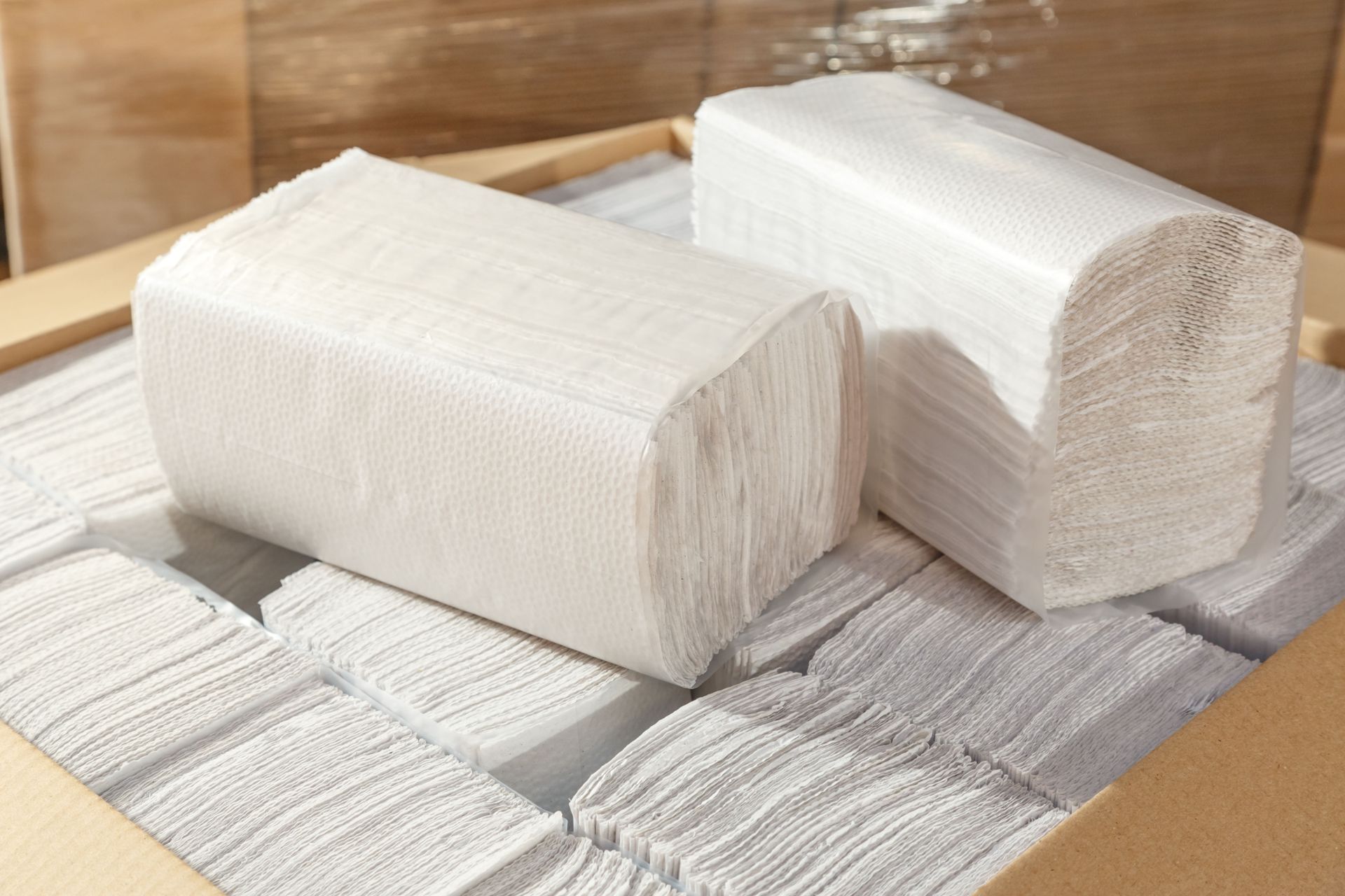 Two stacks of white paper towels in a wooden box, showing folded edges.