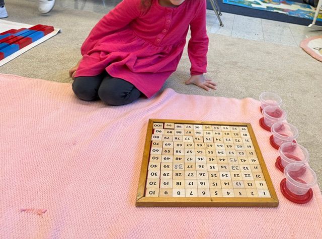 A little girl in a pink dress sits on the floor next to a board with numbers on it