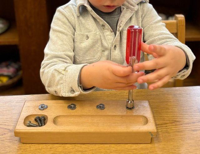 A child is playing with a screwdriver on a wooden board