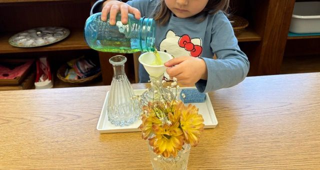 A little girl is pouring liquid into a vase of flowers