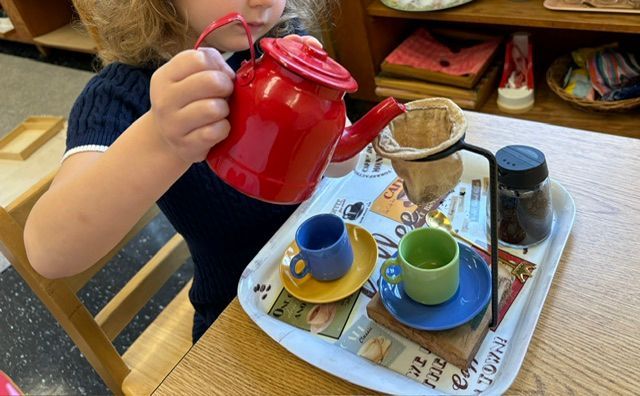 A child is pouring tea into a cup on a tray