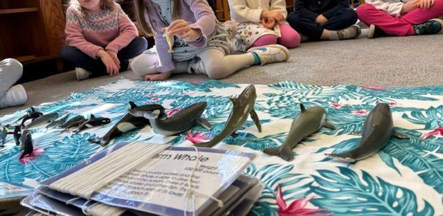 A group of children are sitting on the floor surrounded by toy sharks