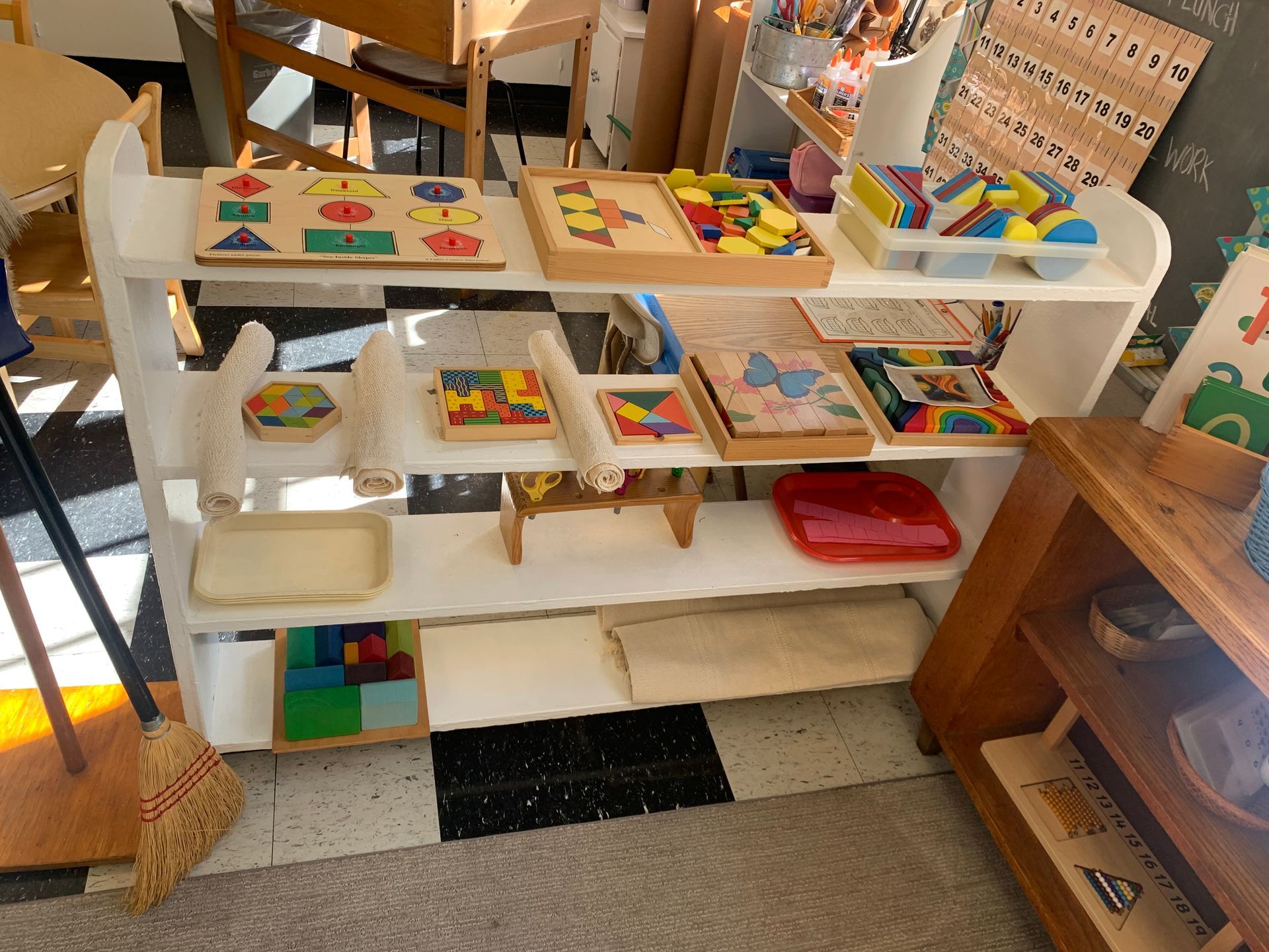 A shelf filled with toys and a broom on the floor