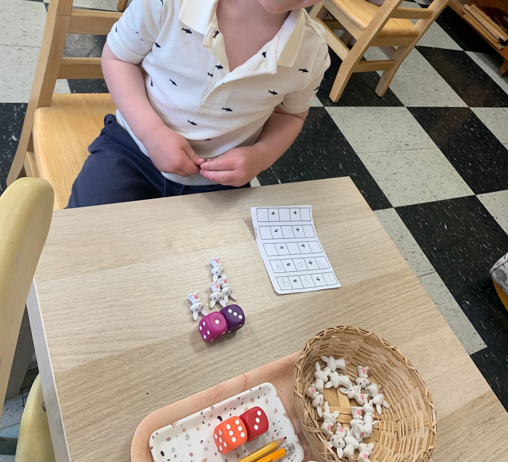 A young boy is sitting at a table with a tray of dice