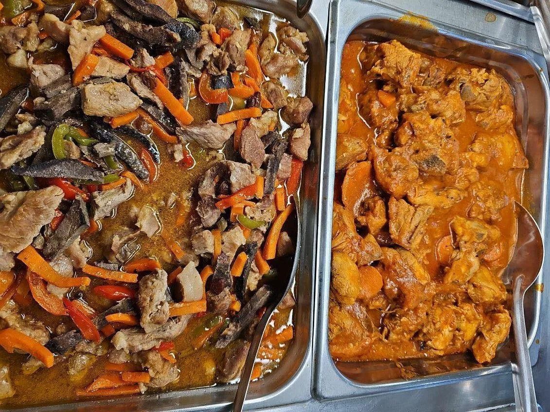 Two metal trays filled with food: one with meat, carrots, and vegetables, and another with orange sauced chicken.