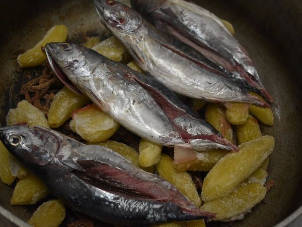 Four whole fish with open bellies sit atop sliced yellow potatoes in a pot.