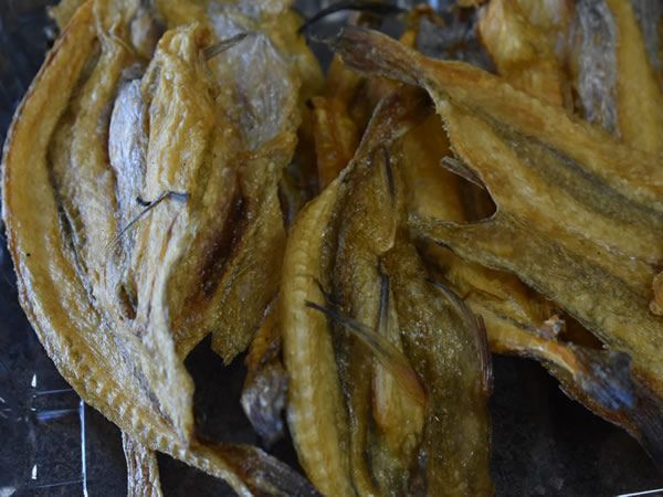 Dried fish, close-up. Yellowish-brown color, thin and flat, with visible spines.