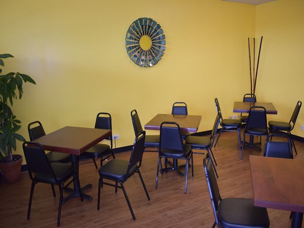 Restaurant dining area with yellow walls, dark tables, and black chairs. Bamboo stalks and a circular art piece are visible.