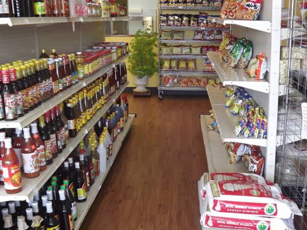 Interior of a small grocery store. Shelves stocked with Asian food products. Wooden floor and plant.