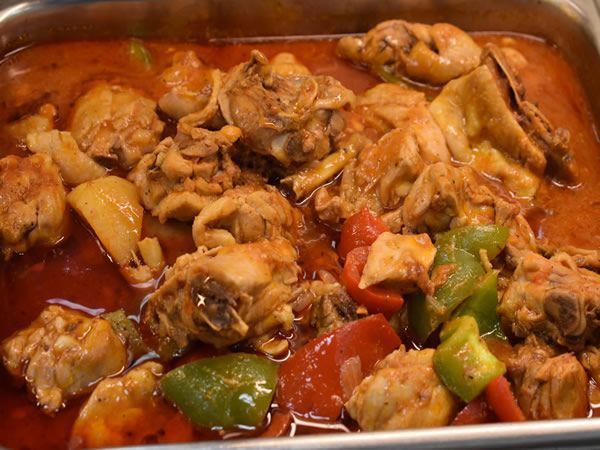 Chicken stew with tomatoes and bell peppers in a metal tray.