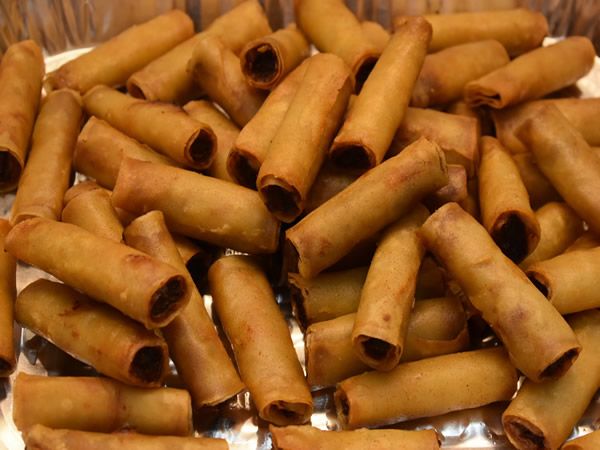 Golden-brown spring rolls piled in a silver container, ready to eat.