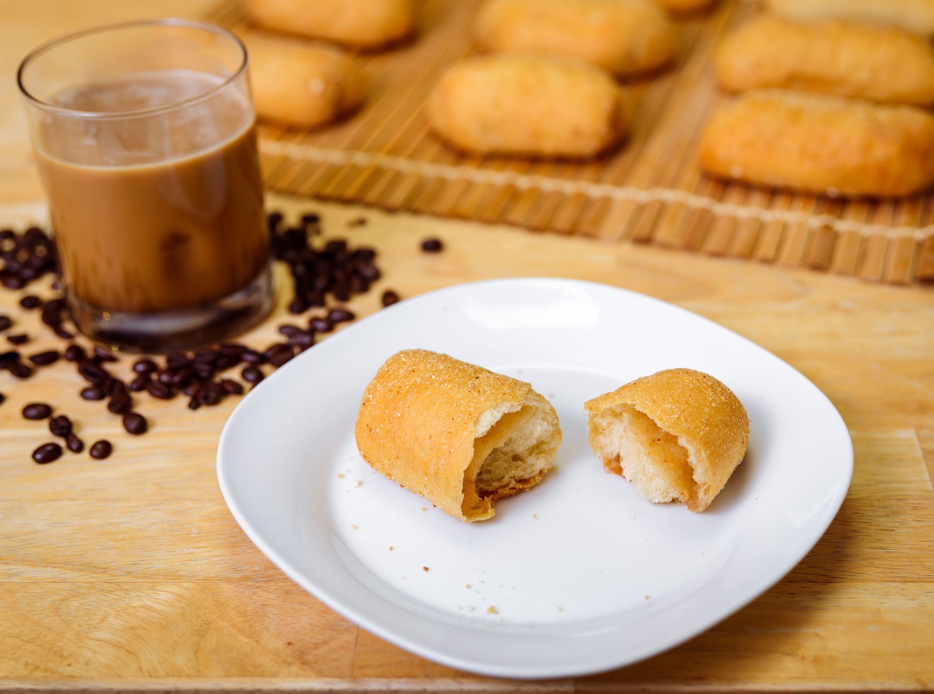 Fried bread rolls with coffee, one cut open on a plate. Coffee beans, and more rolls are on a wooden board.