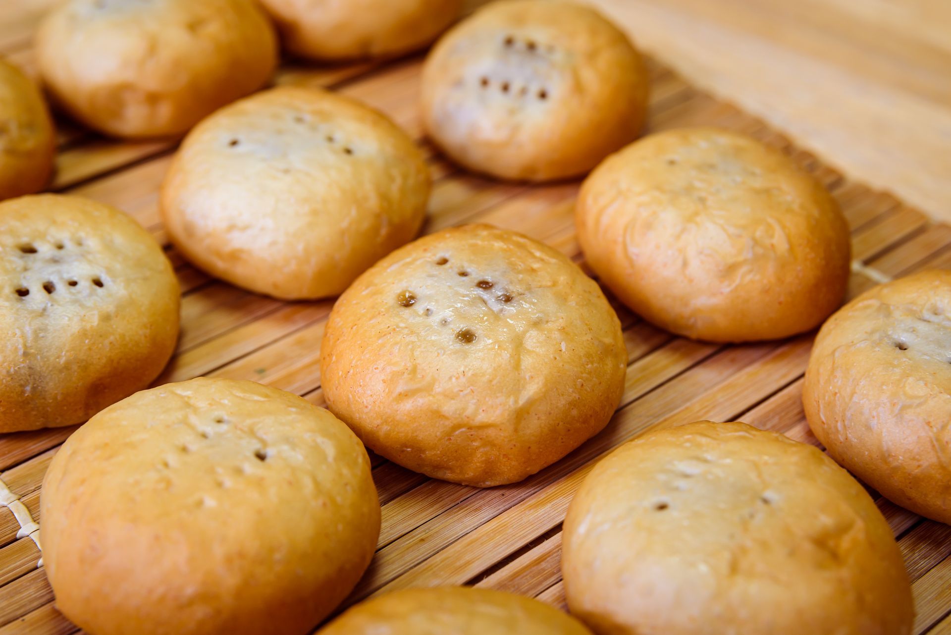 Golden-brown, round pastries with small holes, arranged on a bamboo mat.