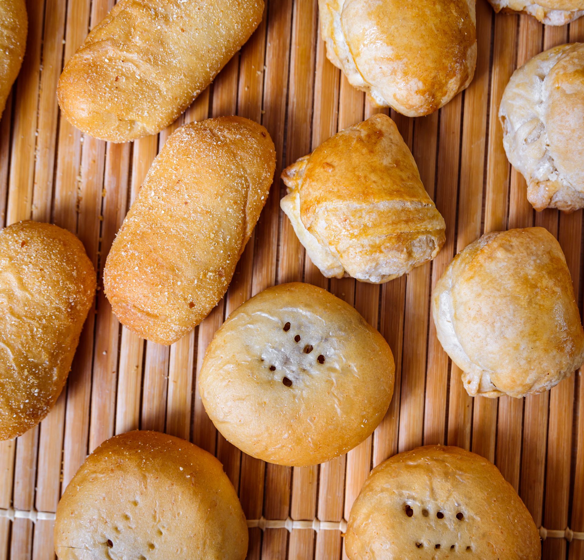 Assorted baked pastries on a light brown bamboo mat; golden-brown color.