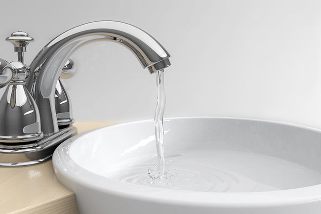 A chrome bathroom faucet with water flowing into a white porcelain sink.