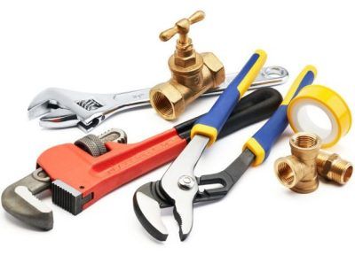 A collection of plumbing tools, including an adjustable wrench, pipe wrench, pliers, a brass valve, fittings, and tape.