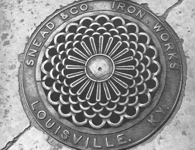 A circular metal grate with an intricate floral pattern, inscribed 