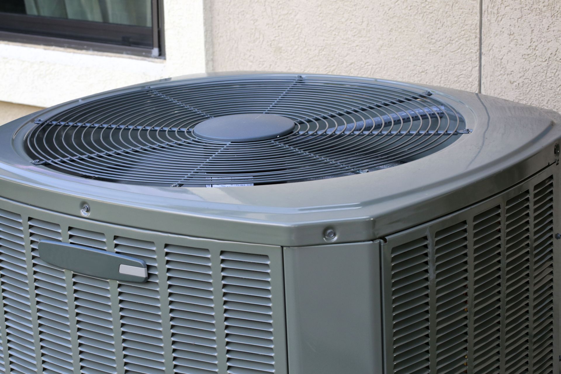 A gray outdoor HVAC condenser unit positioned next to a building wall.