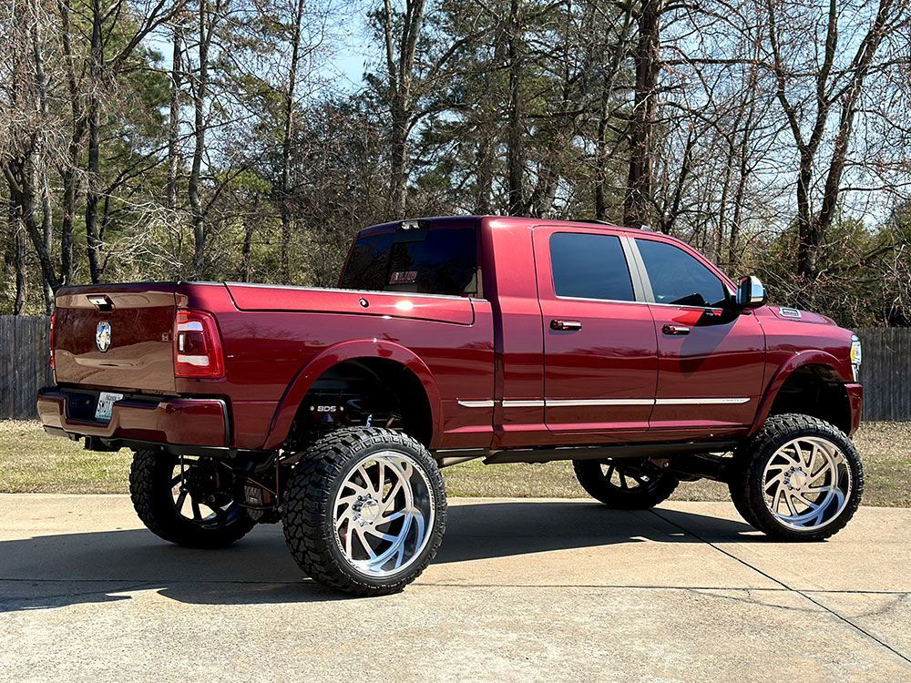 Red lifted pickup truck with large chrome wheels parked outside on a sunny day.